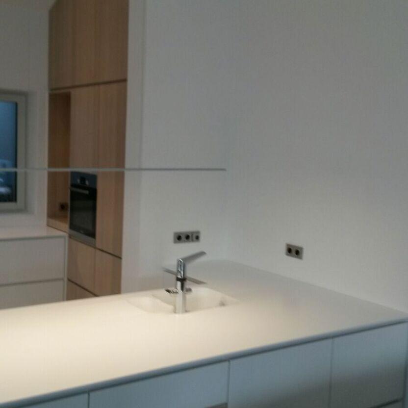 Moderne Kücheninsel mit Spüle Weiße Kücheninsel mit integriertem Spülbecken und schlichter Armatur vor Holzhochschrank