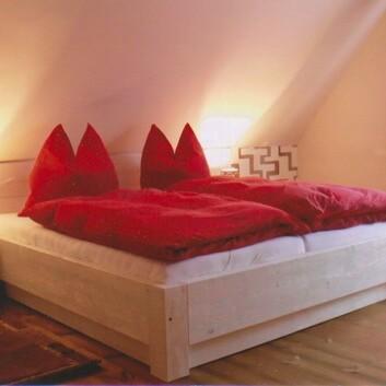 Doppelbett mit roter Bettwäsche Massivholzbett mit roter Bettwäsche, Nachttischen und warmem Licht unter Dachschräge