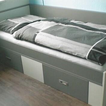 Einzelbett mit Schubladen Graues Einzelbett mit schwarzer Bettwäsche und drei integrierten Schubladen im Unterbau