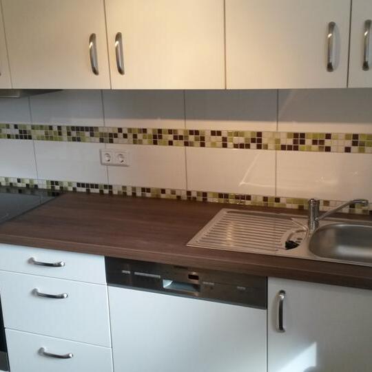 Küchenzeile mit Fliesenspiegel Weiße Küchenzeile mit Holzarbeitsplatte, Mosaik-Fliesenspiegel, Spüle und Einbaugeräten