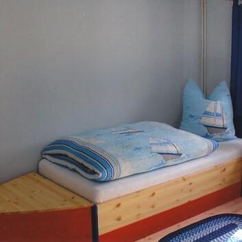 Kinderbett in Bootsform Holzbett in Bootsform mit maritimer Bettwäsche, blauer Vorhang und Nachttischlampe