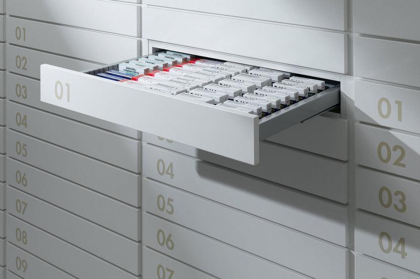 Detailaufnahme von schmalen weißen Medikamentenschubläden mit dezenter Nummerierung und sichtbarer Medikamentenaufteilungen.