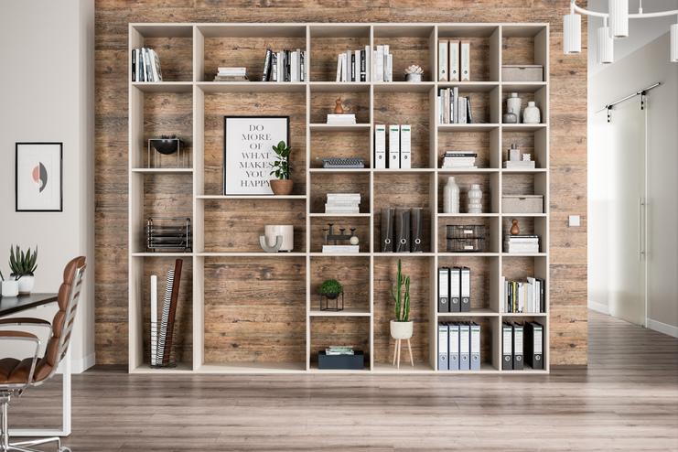 Ein großes, helles Regal nach Maß, gefüllt mit Büchern und Dekorationen, vor einer Wand mit Holzoptik.