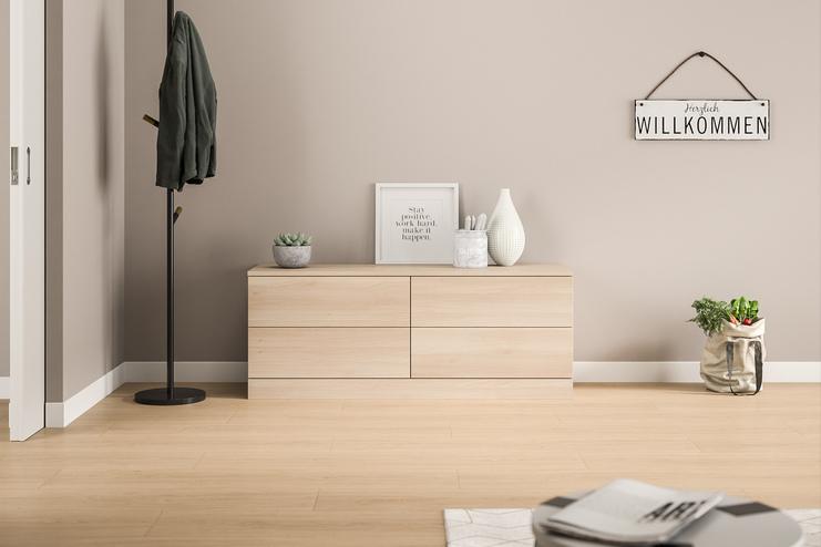 Eine schlichte, maßgeschneiderte Kommode in hellem Holzdekor mit glatten Fronten, harmonisch integriert in den einladenden Eingangsbereich eines Hauses.